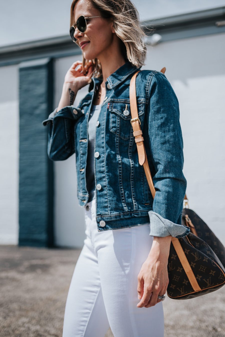 Suzanne wearing white denim jeans, a denim jacket, and carrying a Louis Vuitton bag