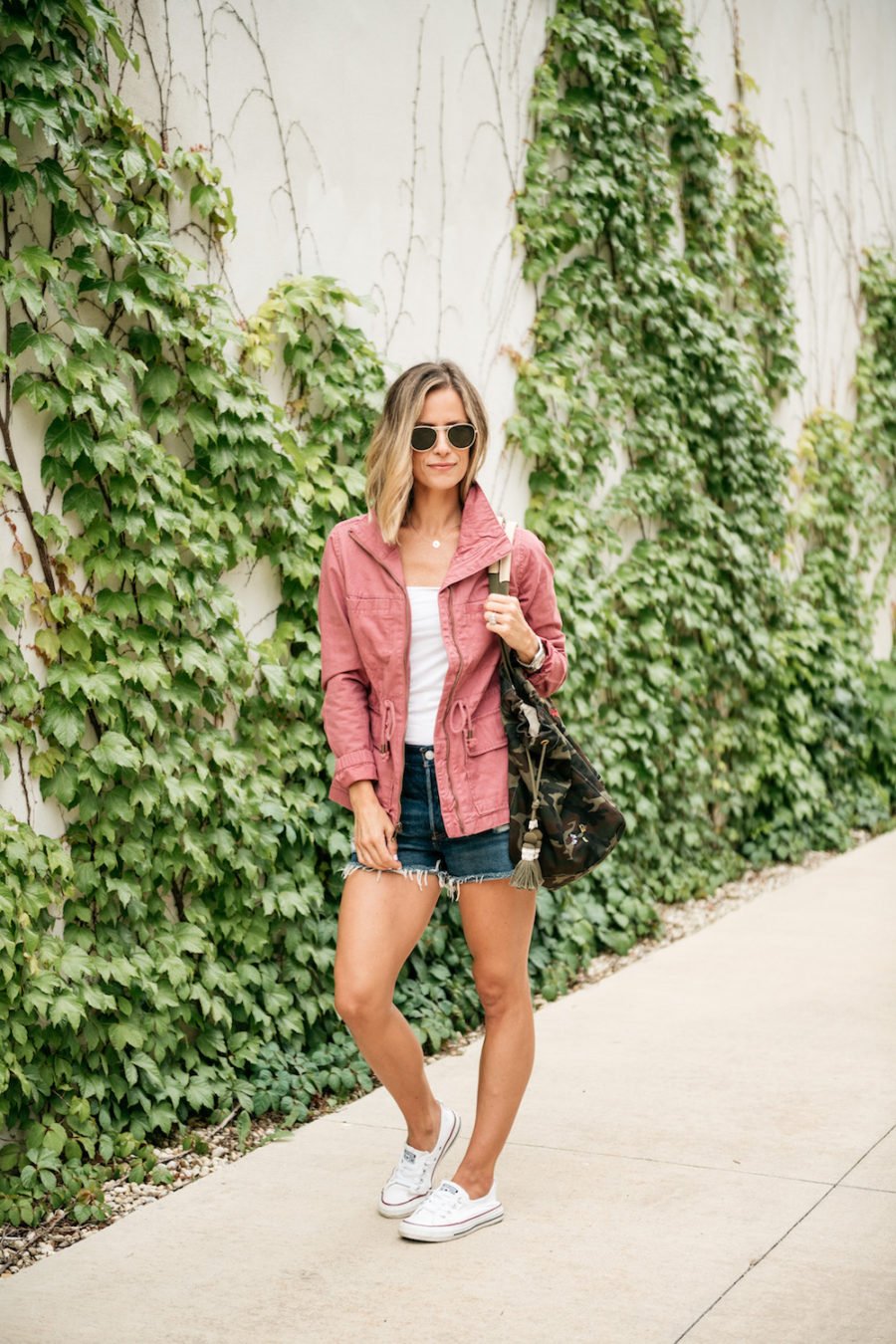 Pink jacket, white tee, denim shorts, camo tote, and Coverse