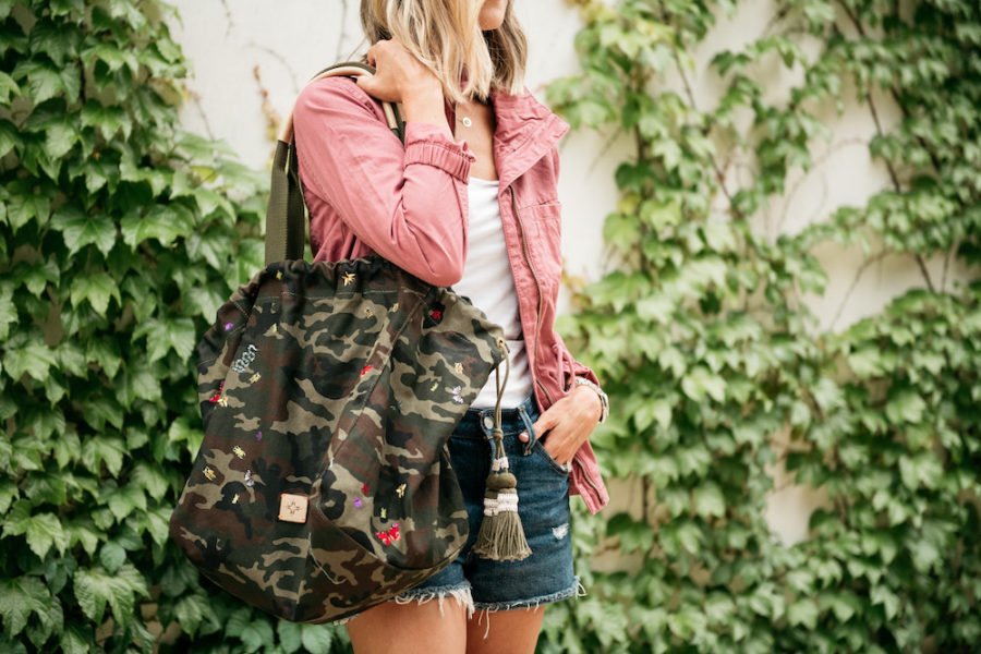 Pink jacket, white tee, denim shorts, camo tote, and Coverse