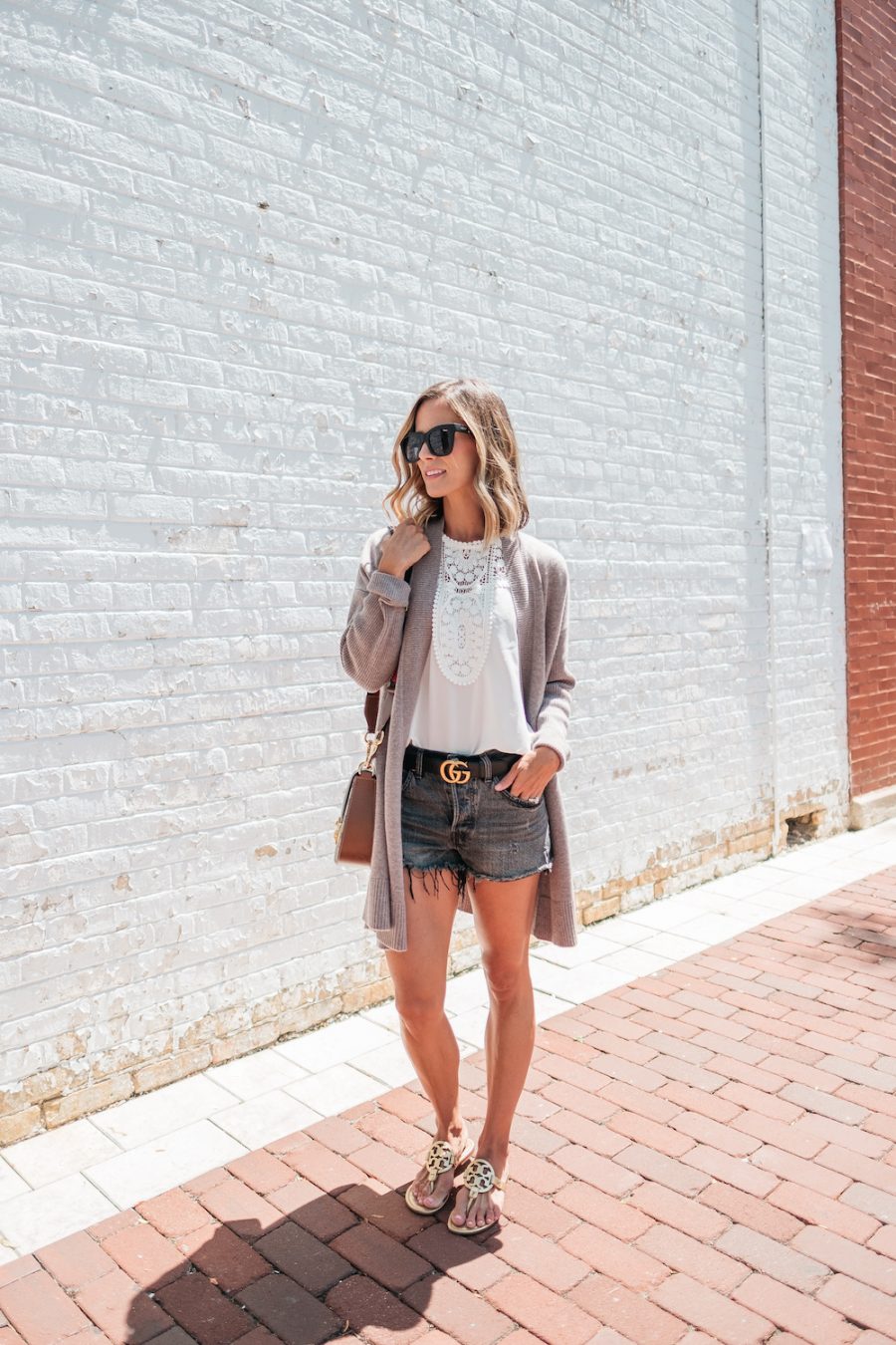 Suzanne wearing a white lace blouse, cardigan, denim shorts, and sandals