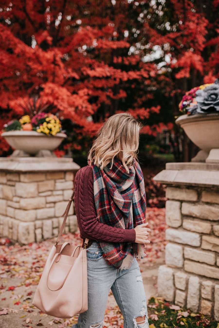 Thanksgiving outfit ideas: Suzanne wearing a burgundy sweater, plaid scarf, denim jeans, and pink tote