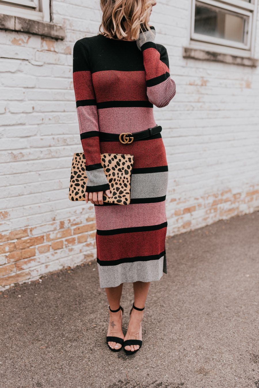 Suzanne wearing a sweater dress, black heels, and a clutch 