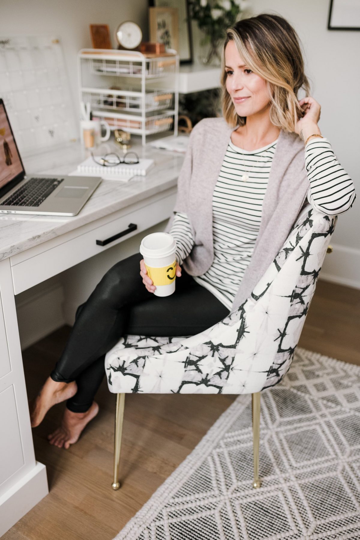 Suzanne sitting at her desk wearing a striped tee, Spanx faux leather leggings, and a cashmere rauna