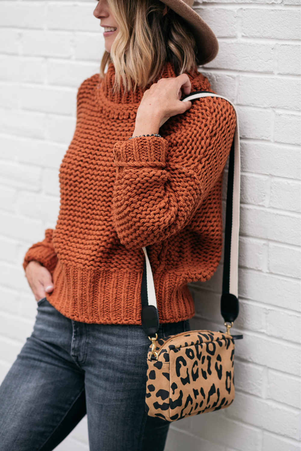 Thanksgiving outfit ideas: Suzanne wearing an orange sweater, denim, and leopard crossbody