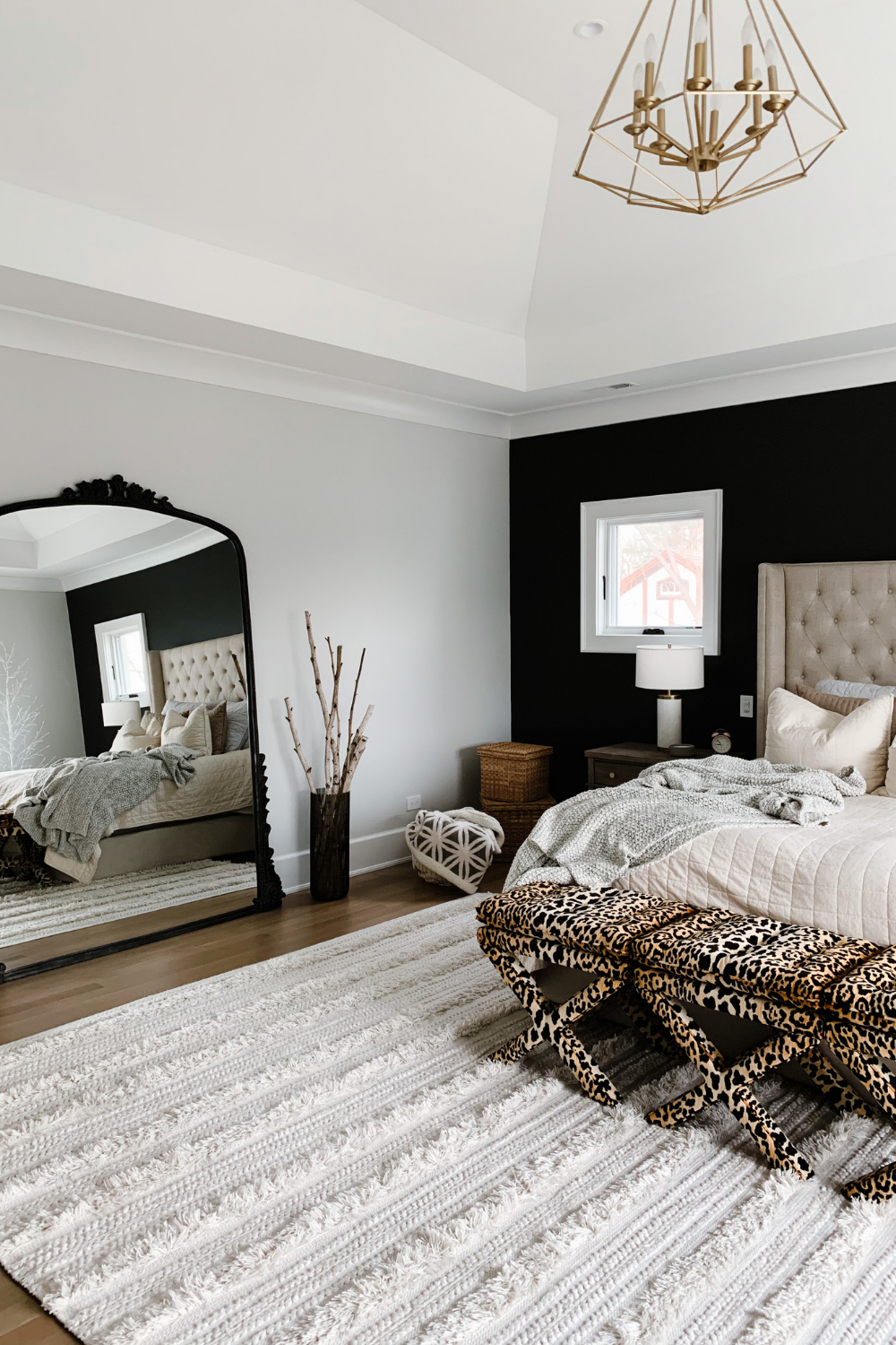 Master bedroom with black accent wall, king bed with neutral bedding, leopard ottomans and a floor length mirror
