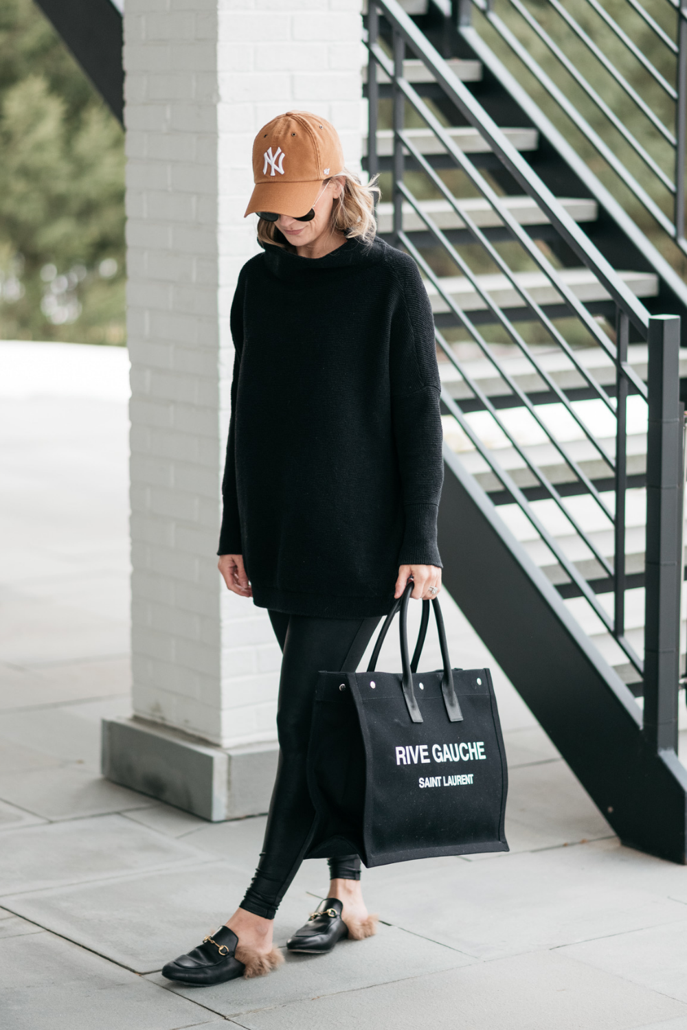 Suzanne wearing a tunic, faux leather leggings, a baseball cap, tote, and mules