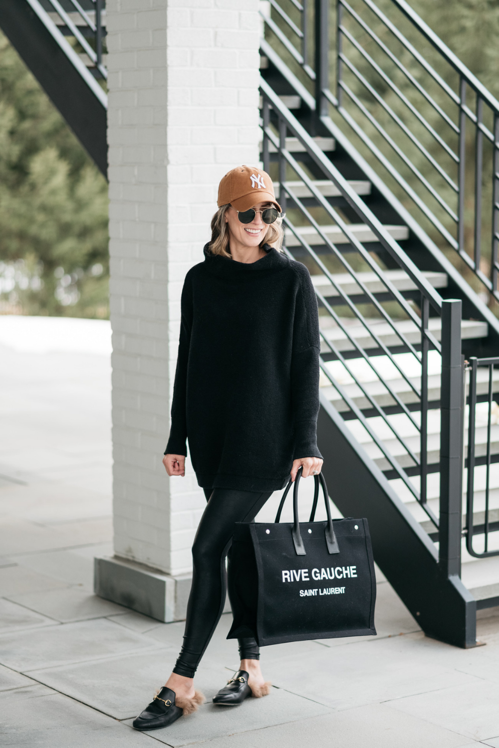 Suzanne wearing a black tunic, Spanx leggings, mules, a tote