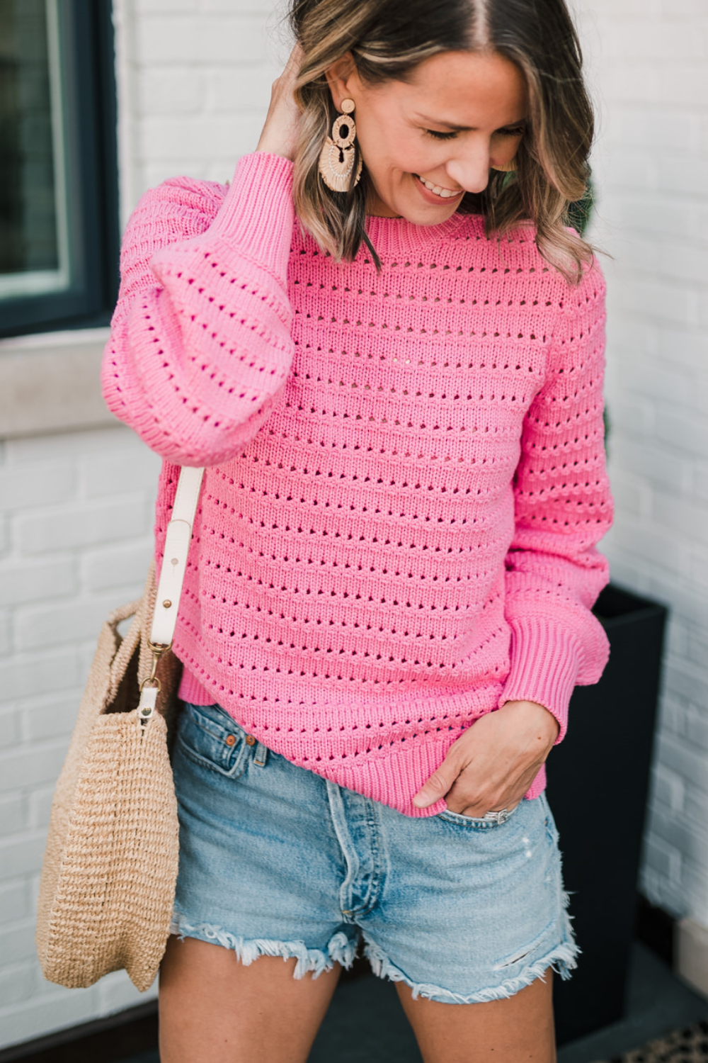 Suzanne wearing a pink sweater, denim shorts, and a round bag