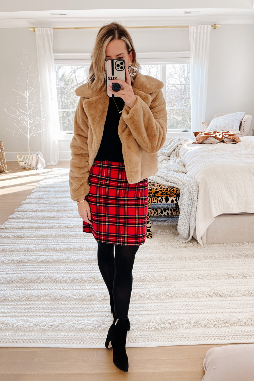 Suzanne wearing a red plaid pencil skirt, black top, faux fur jacket, tights and booties