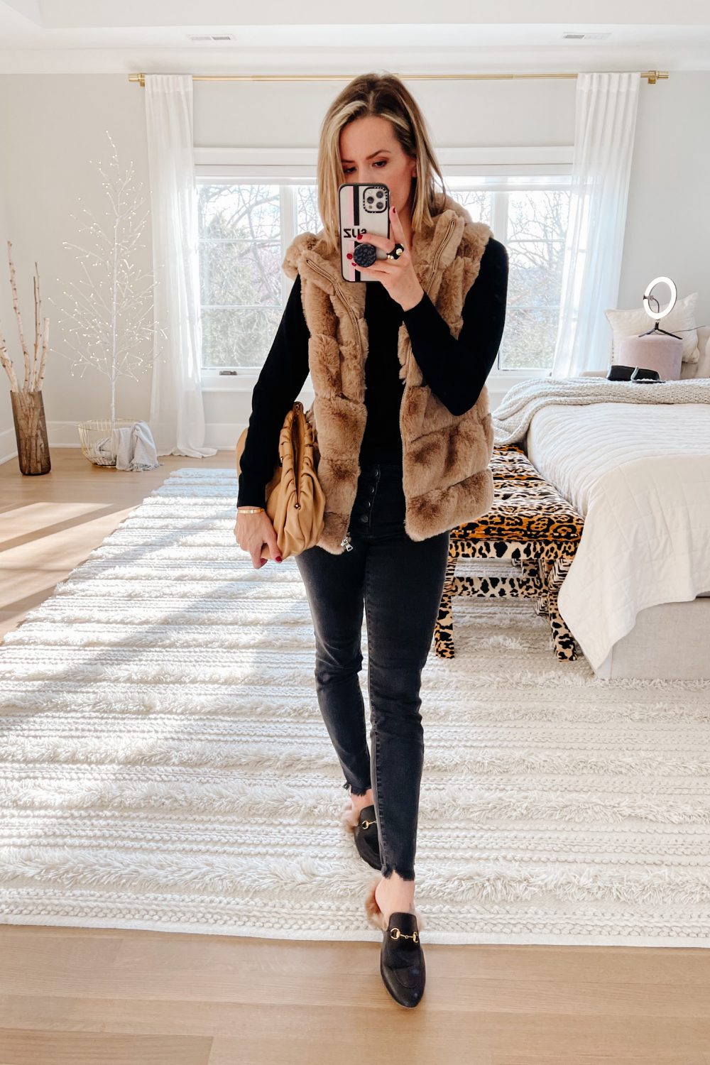 Suzanne wearing a black long sleeve tee, black denim, a fur vest, clutch ad loafers
