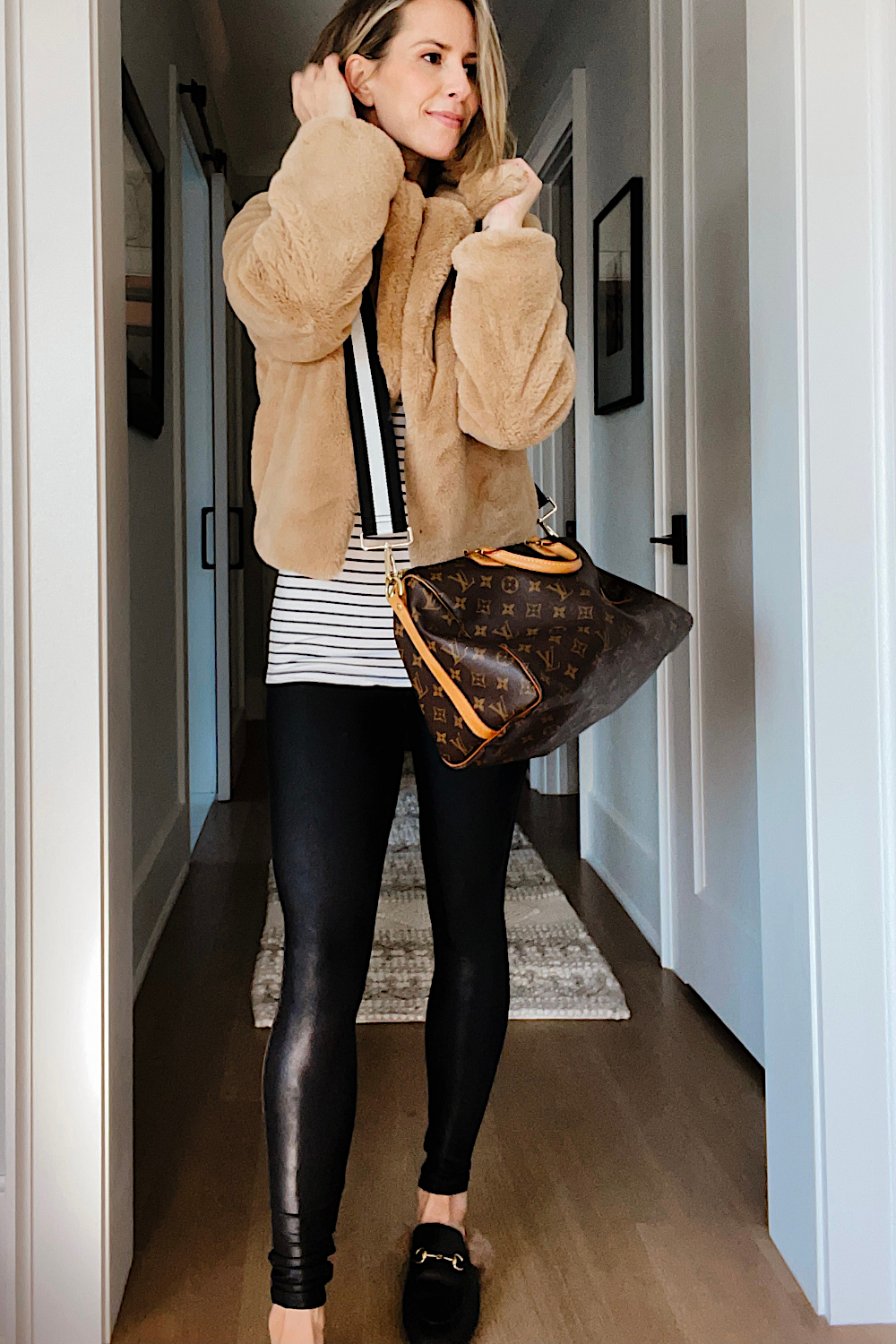 Suzanne wearing a faux fur jacket, striped tee, Spanx faux leather leggings, and a Louis Vuitton handbag