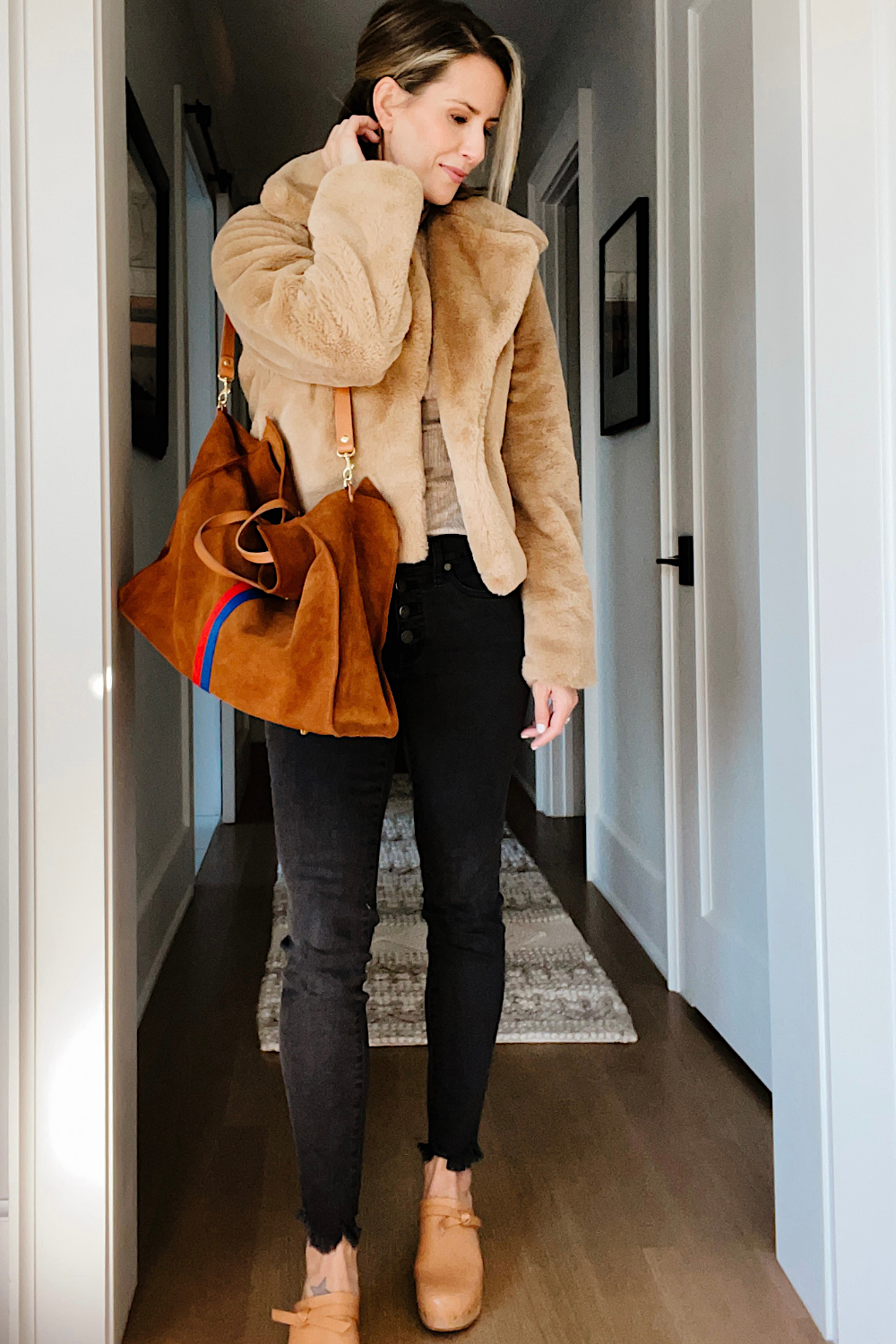 Suzanne wearing a faux fur jacket, black skinny jeans, and brown suede tote