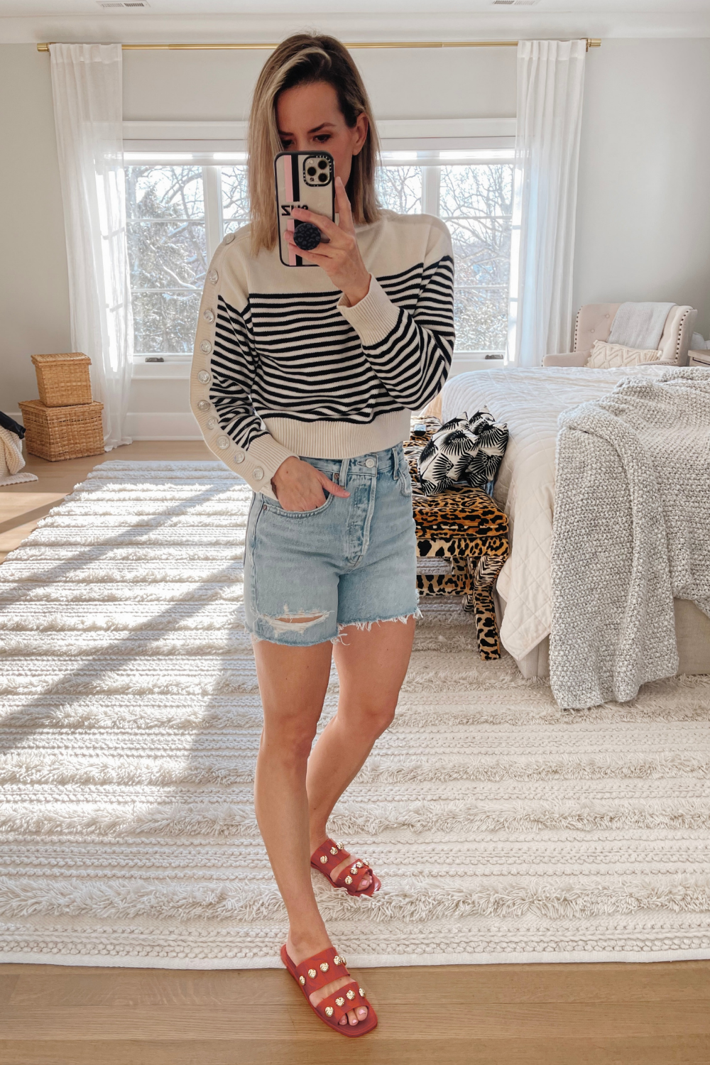 Suzanne wearing a striped sweater, denim shorts, and sandals