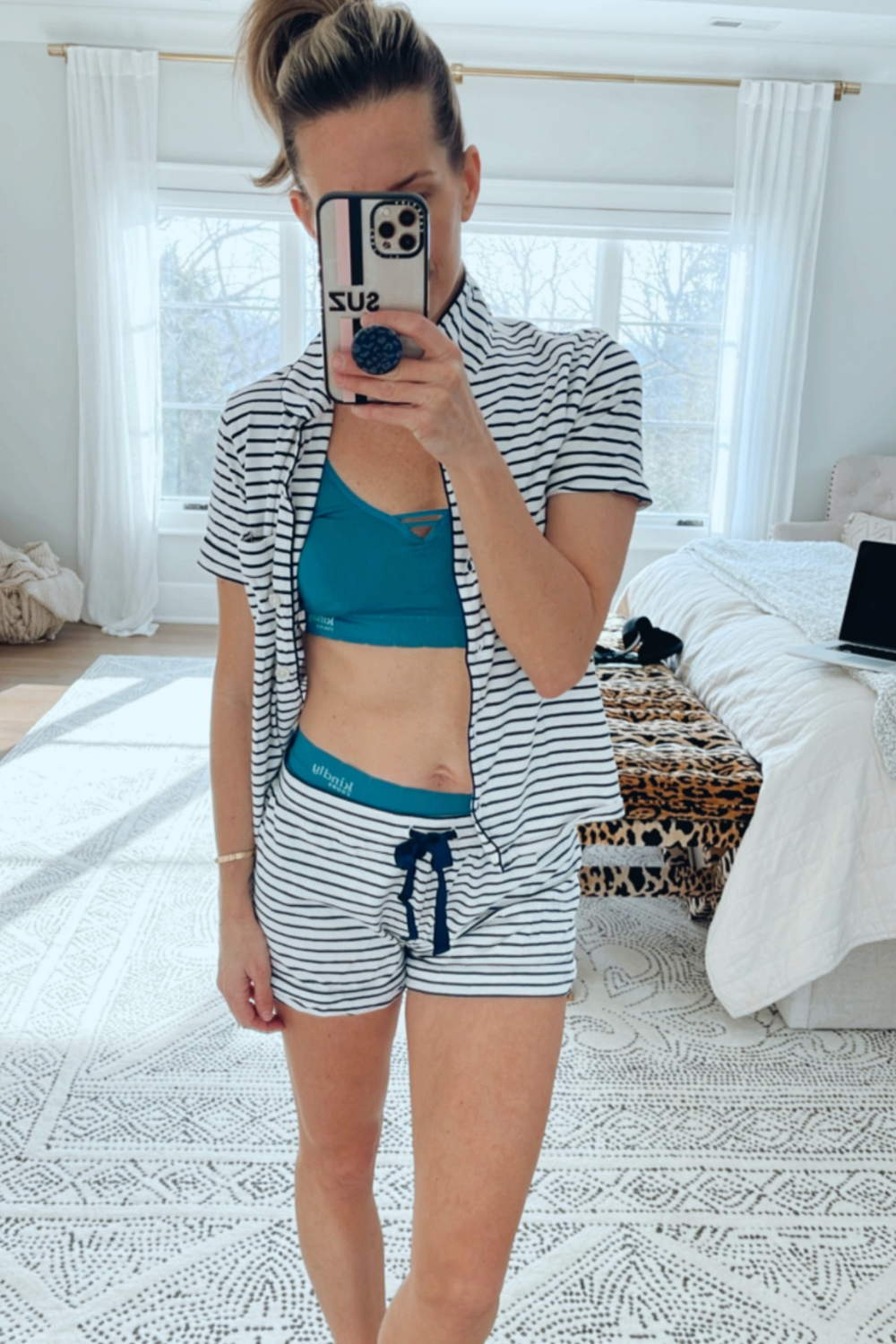 Suzanne taking a mirror selfie in a striped shorts pajama set and a Kindly sustainable bra and underwear set.