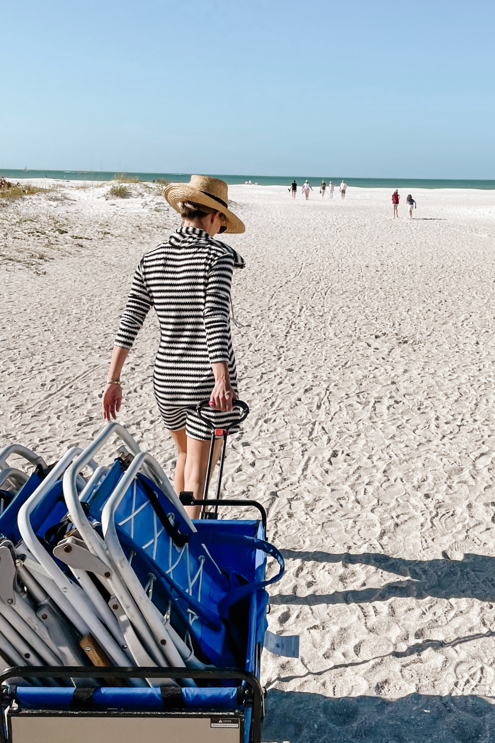 Suzanne pulling a wagon on the beach in a striped cover up. 