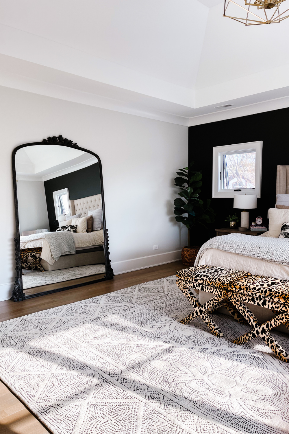 Master bedroom with black accent wall, printed area rug, leopard ottomans, and a black floor length Anthropologie mirror
