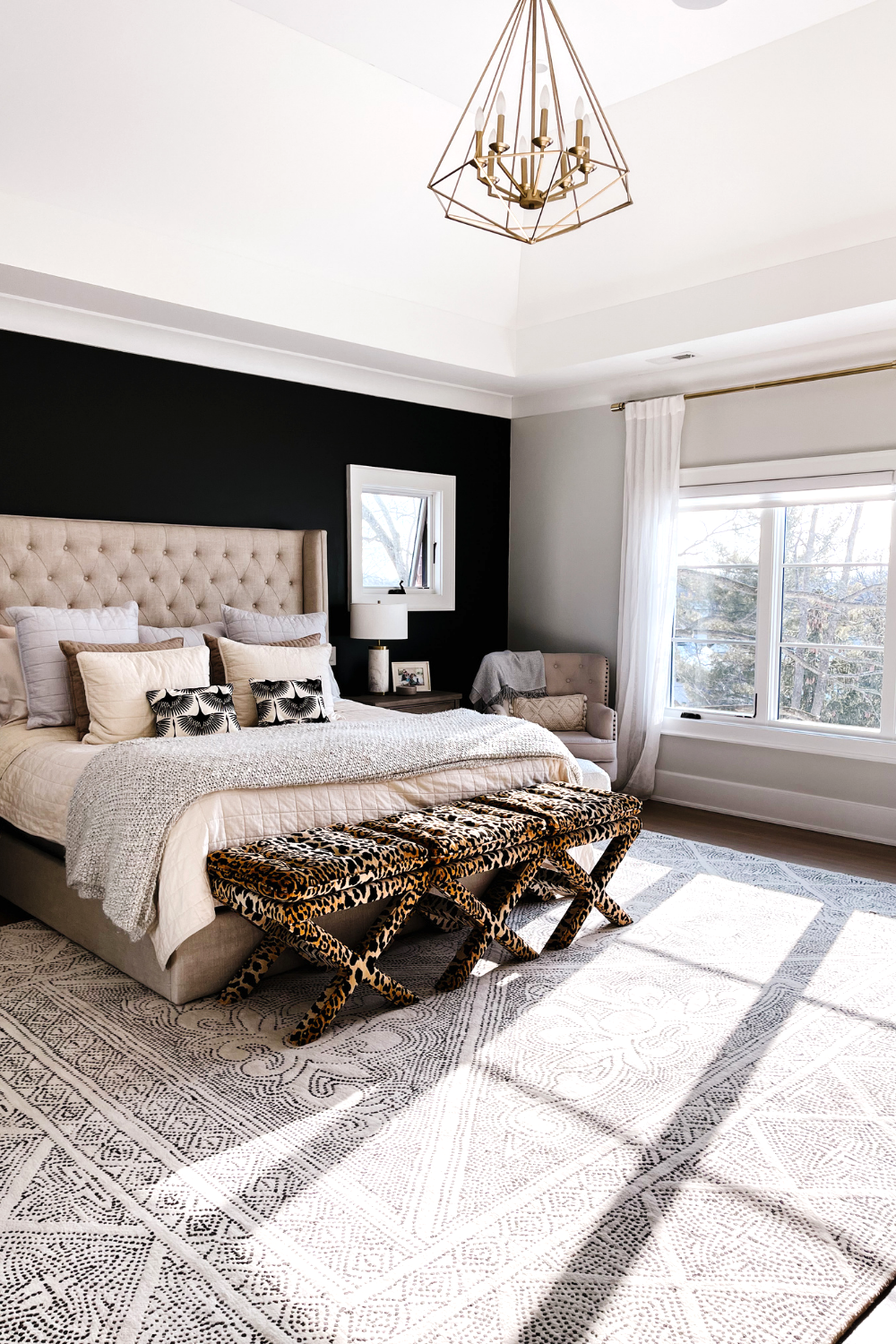 Master bedroom with black accent wall, tufted bed frame, wood side table, printed area rug and reading nook