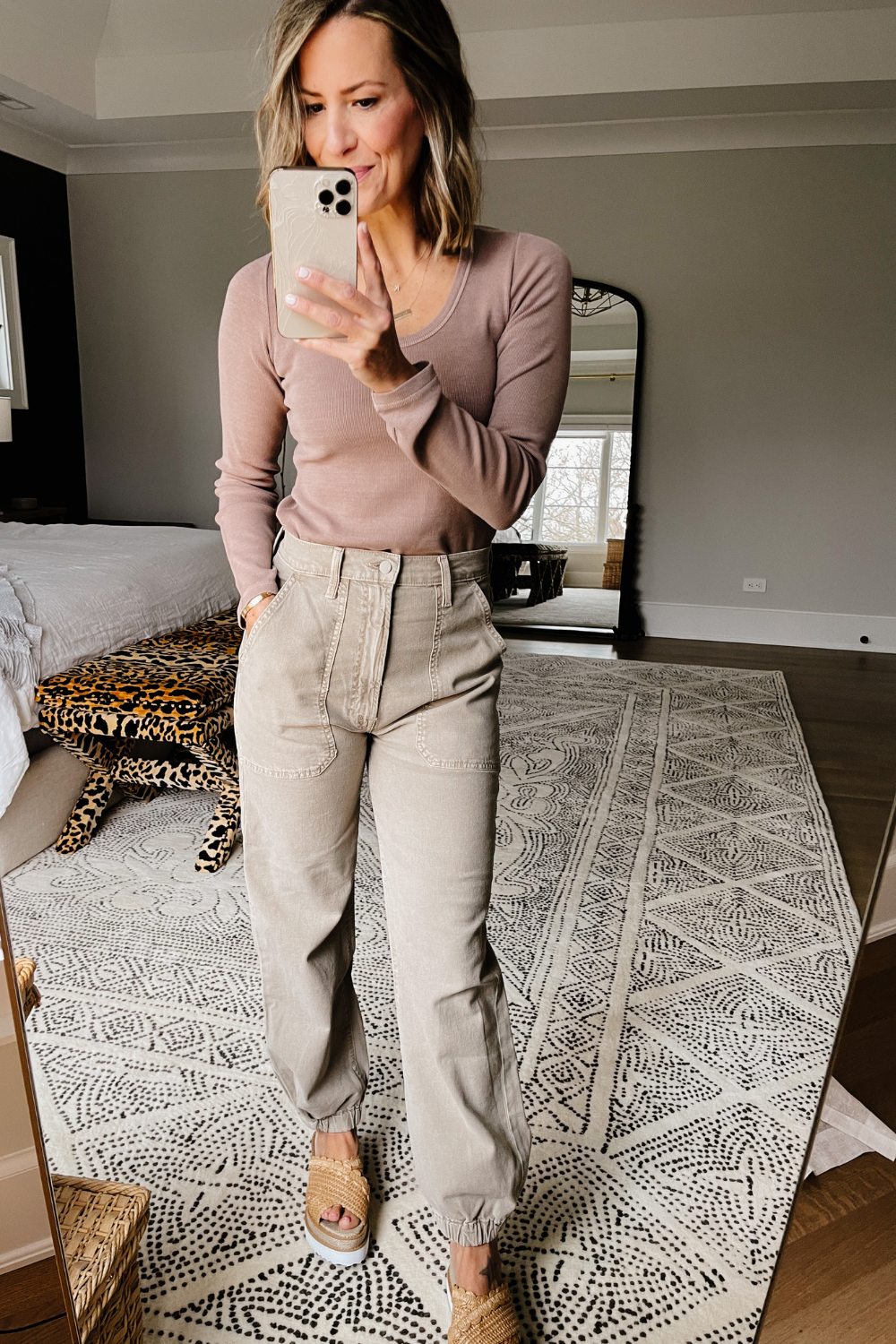 Suzanne taking a mirror selfie wearing a long sleeve top, ankle pants, and wedges. 