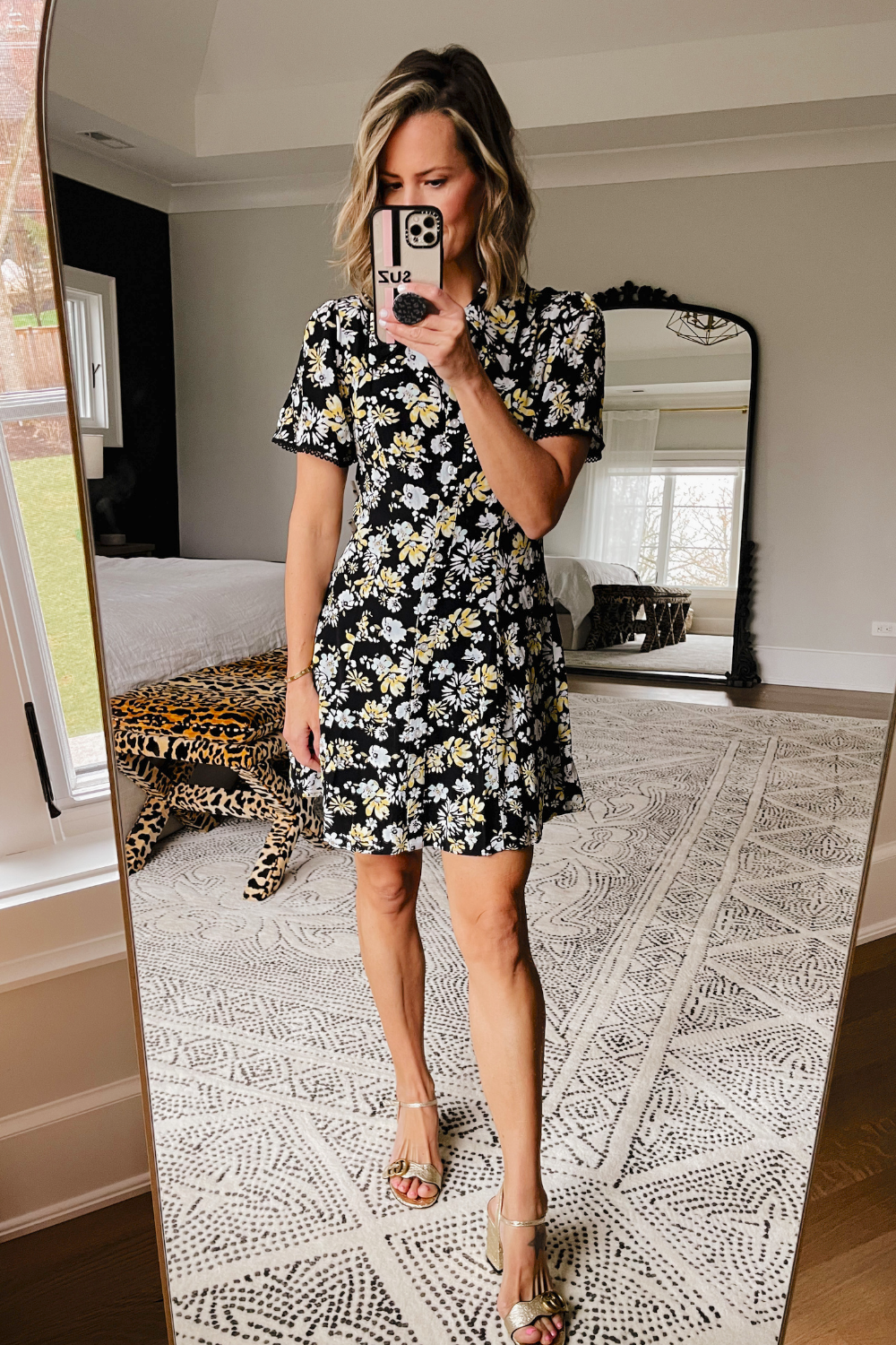 Suzanne taking a mirror selfie wearing a floral printed mini dress and Gucci heels.