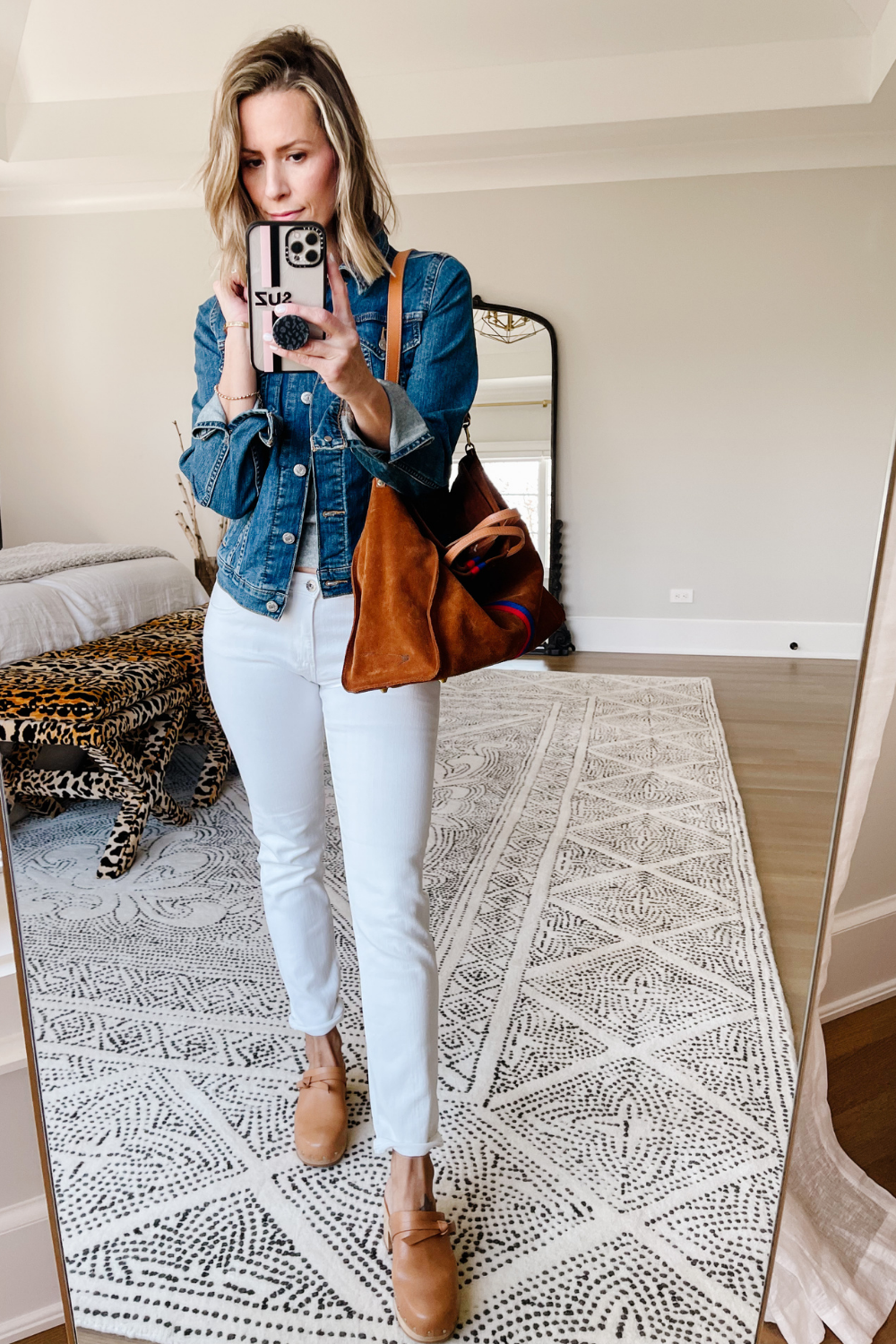 Suzanne wearing white denim jeans, a denim jacket, clogs, and carrying a tote