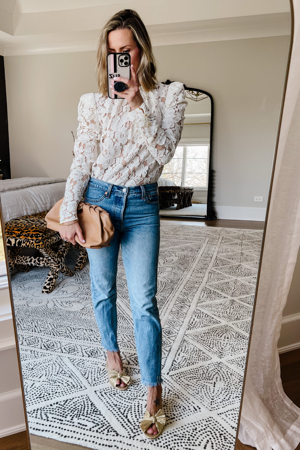 Suzanne wearing a white lace blouse, Levi's wedgie jeans, metallic bow heels, and carrying a clutch 
