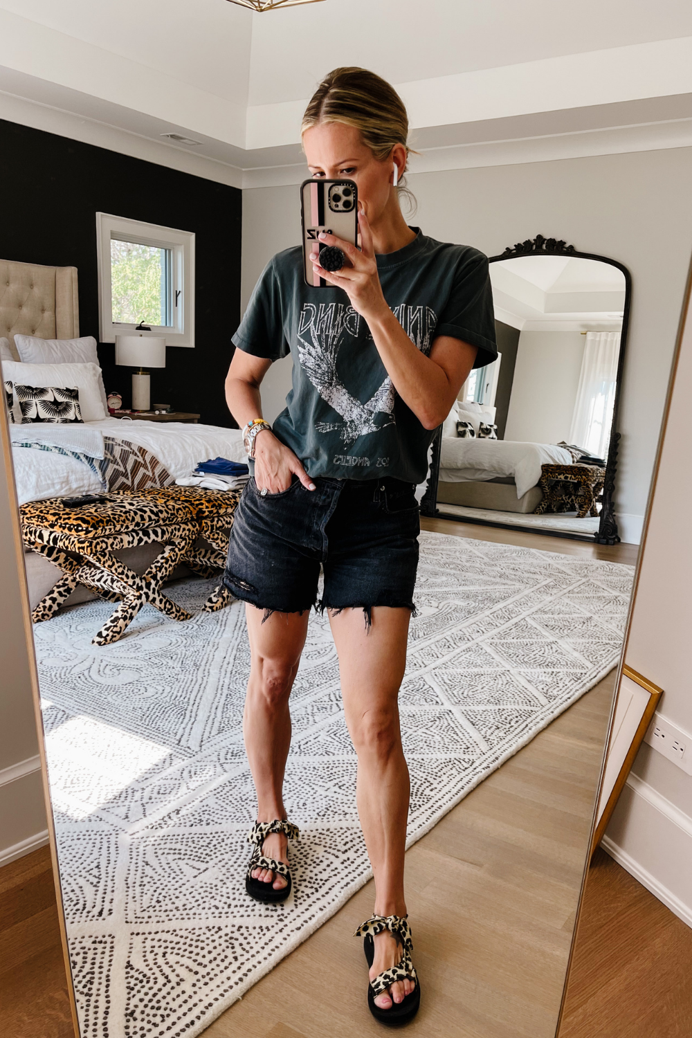 Suzanne wearing a black graphic tee, black denim shorts, and sport sandals 
