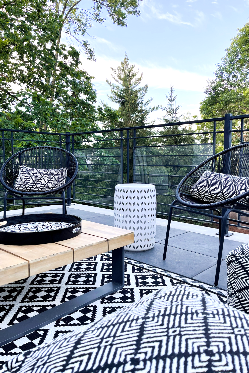 Outdoor seating area with black circle chairs, a printed rug, wood table, and poufs