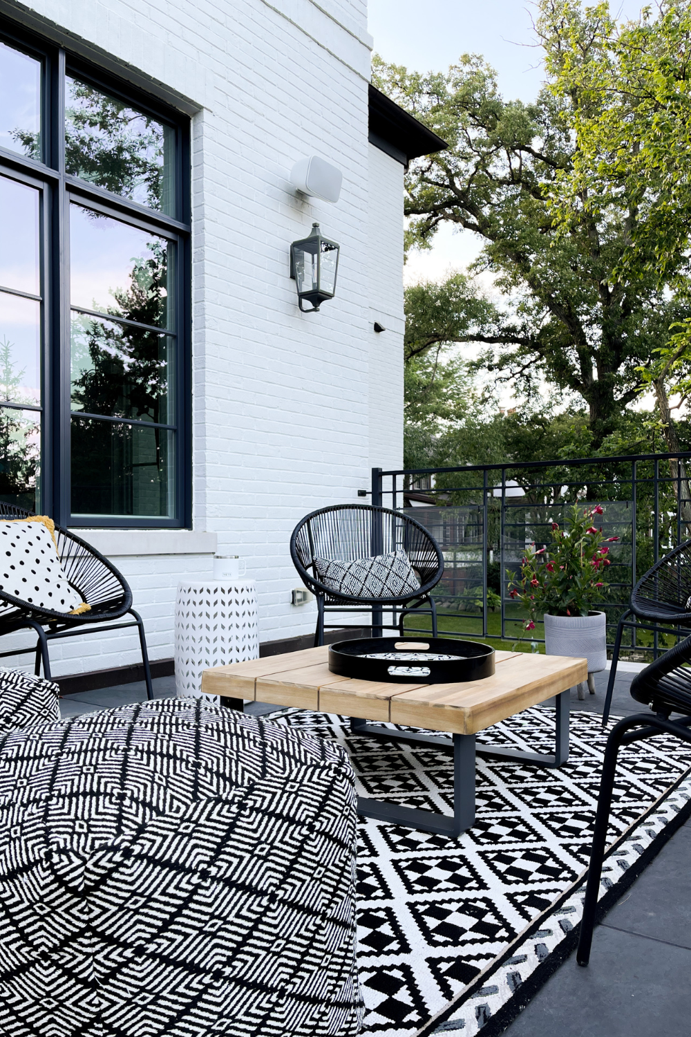 Outdoor seating area with black circle chairs, a printed rug, wood table, and poufs