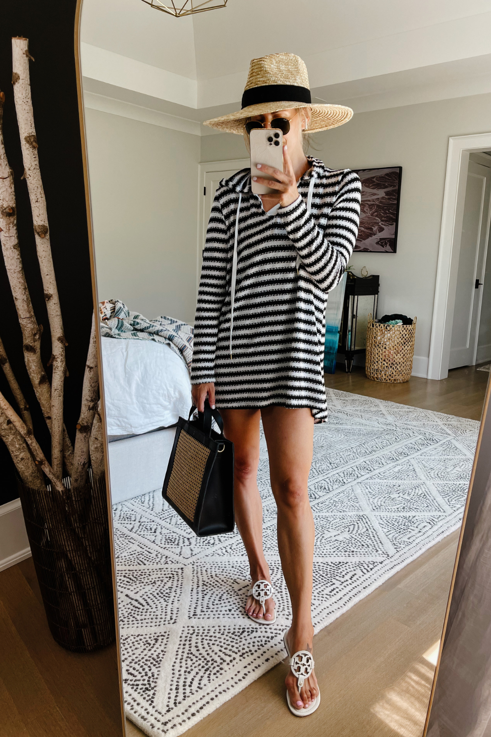 Suzanne taking a mirror selfie in a striped swim cover up, straw hat, wicker bag, and sandals