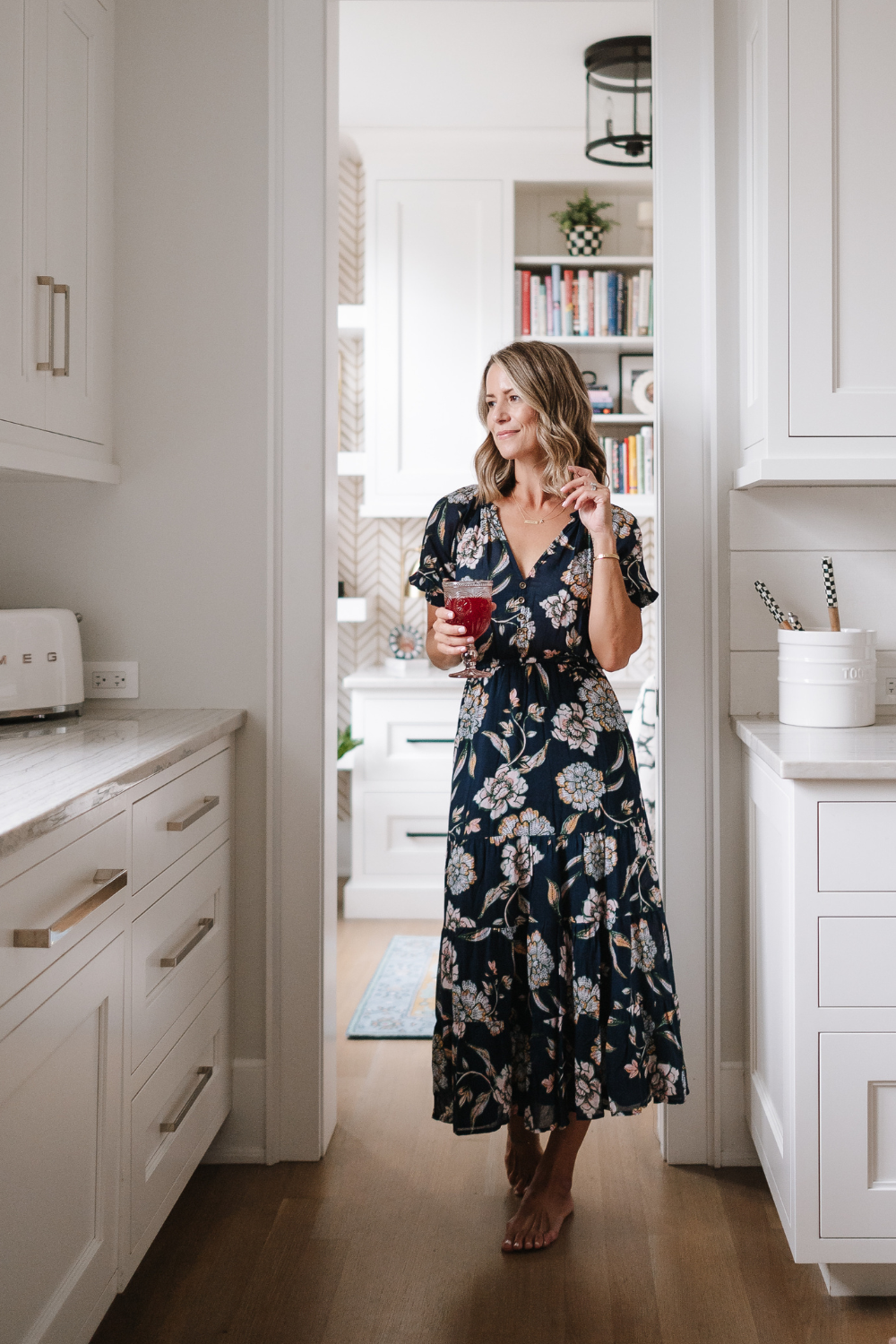 Suzanne wearing a floral printed maxi dress and drinking Kombucha