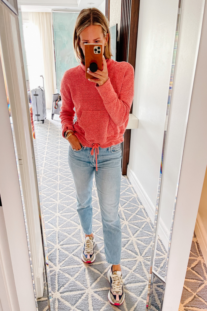 Suzanne taking a mirror selfie in a Sweaty Betty sweater, denim jeans, and sneakers