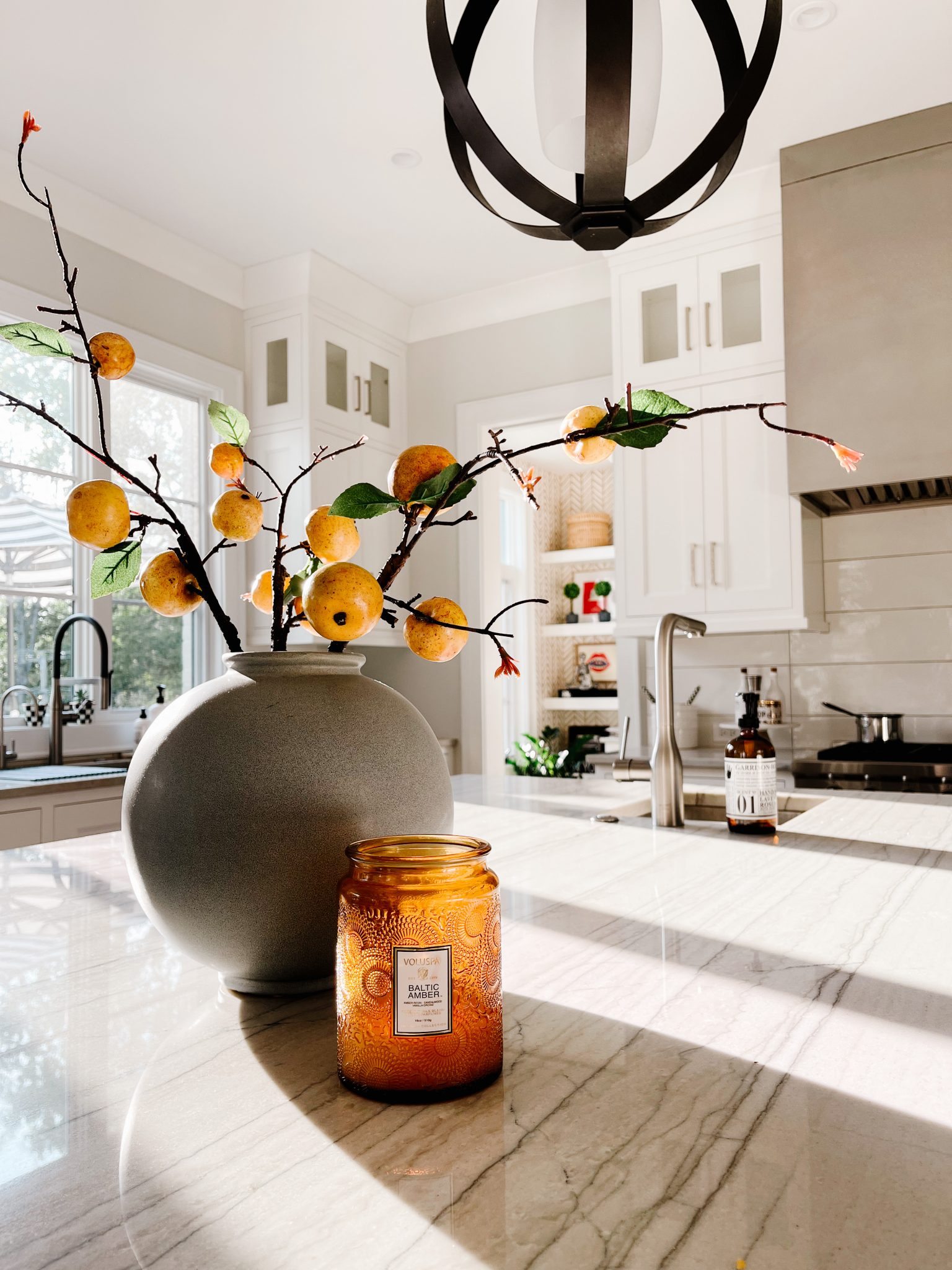 A round blue vase on the kitchen island holding pear branches next to a fall candle. 