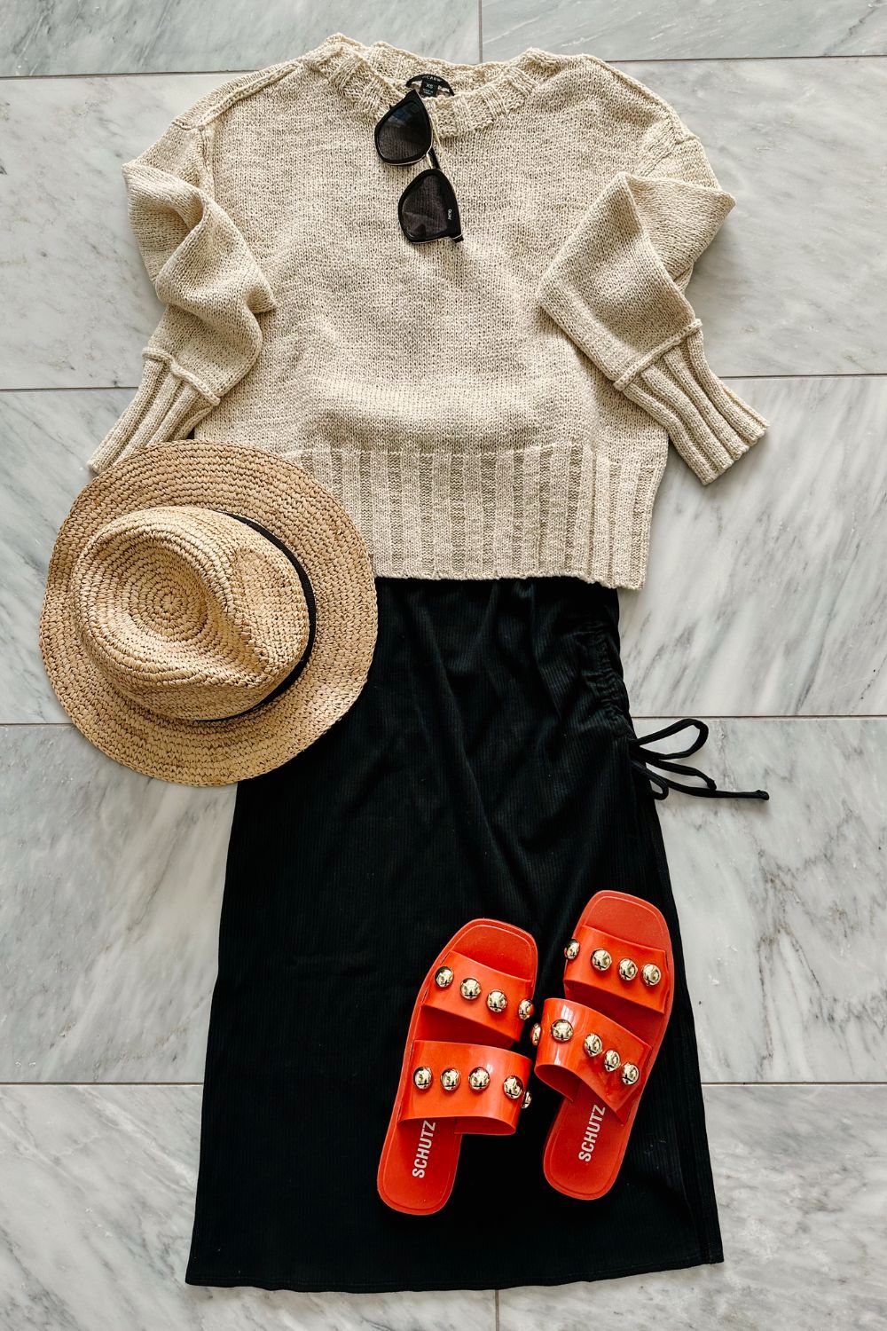 A midi dress styled with a light weight sweater, hat, and sandals 