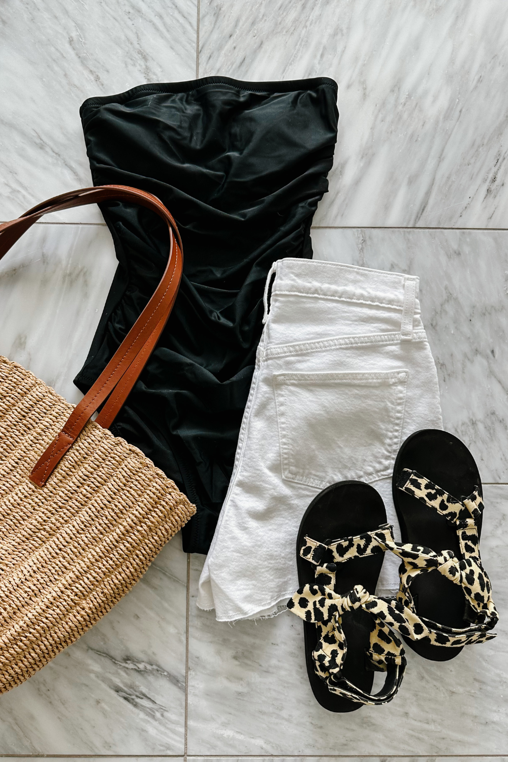 A one piece swimsuit styled with white shorts, a straw bag, and sandals