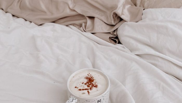 a cup of latte on bed with white linen