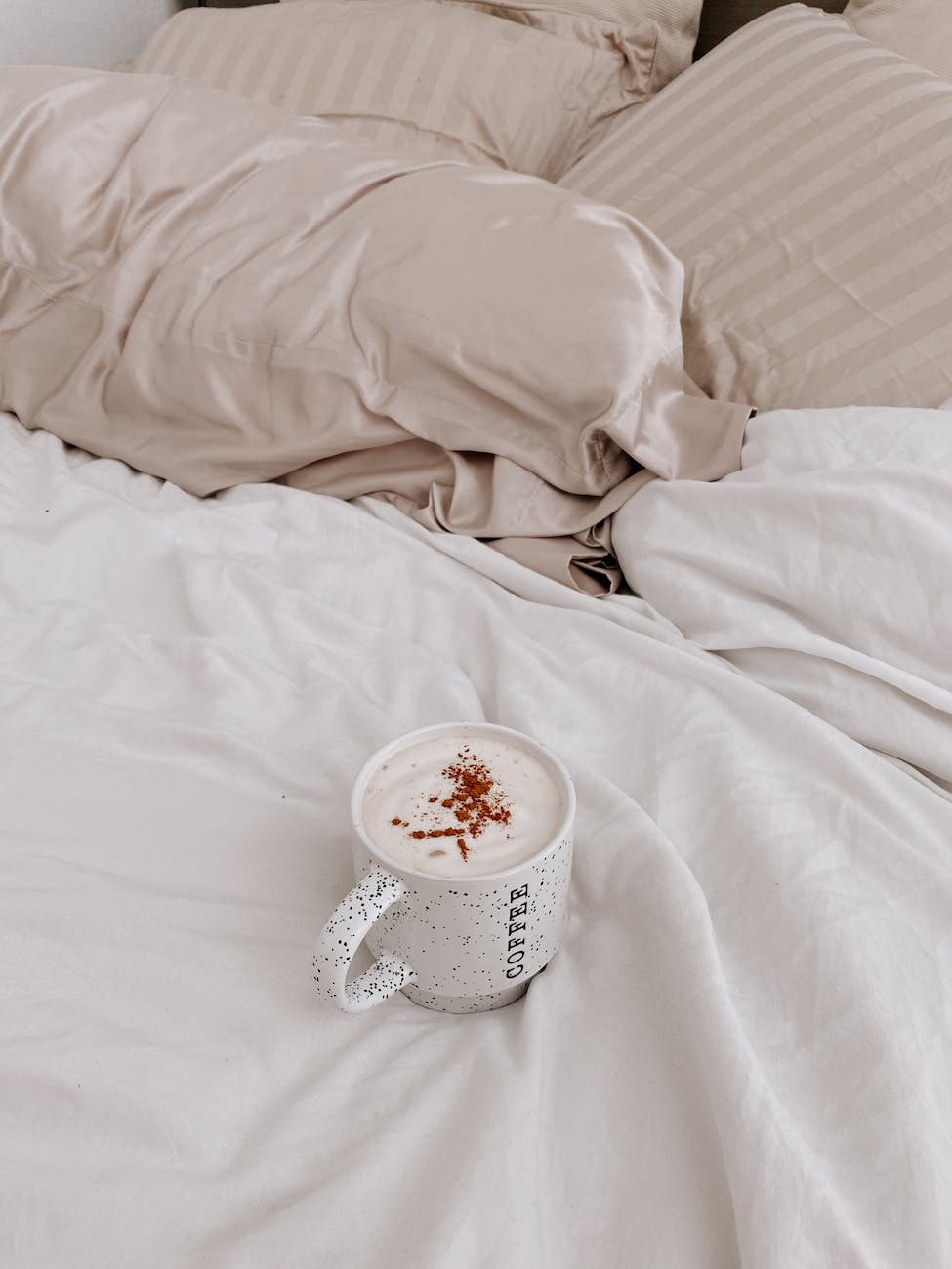 a cup of latte on bed with white linen